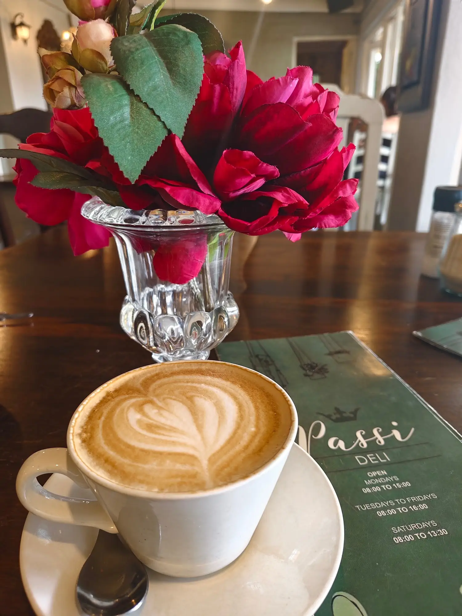 A cappuccino on a floral tablecloth, beside their green menu